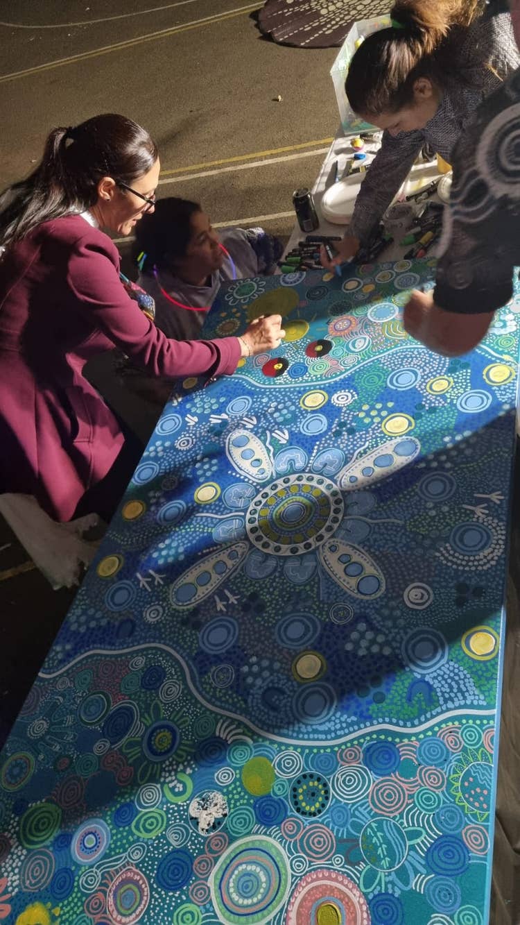 Image of school principal and community members working on an artwork with various blue colours, dots lines and circles