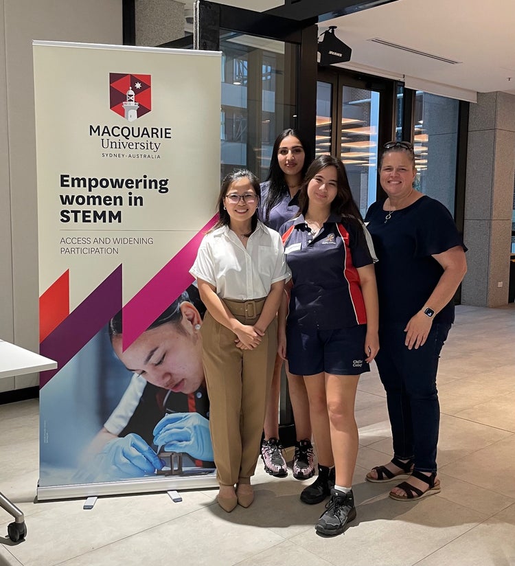 Image infront of Macquarie University sign two students and two staff members